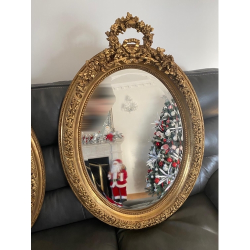 77 - A VERY FINE PAIR OF GILT OVAL SHAPED WALL MIRRORS, the mirrors with bevelled edge, the frames decora... 