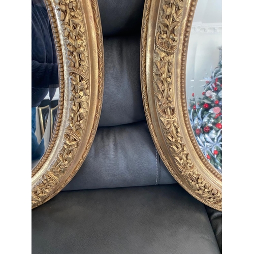 77 - A VERY FINE PAIR OF GILT OVAL SHAPED WALL MIRRORS, the mirrors with bevelled edge, the frames decora... 