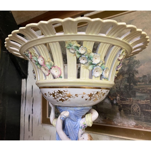 103 - A LARGE PORCELAIN COMPOTE CENTREPIECE, with flower encrusted basket, female figures to column standi... 