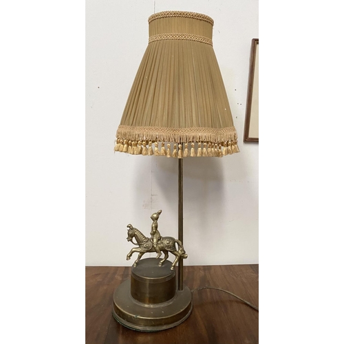 99 - A VINTAGE BRASS TABLE LAMP, with horse and solider atop circular platform base, complete with fringe... 