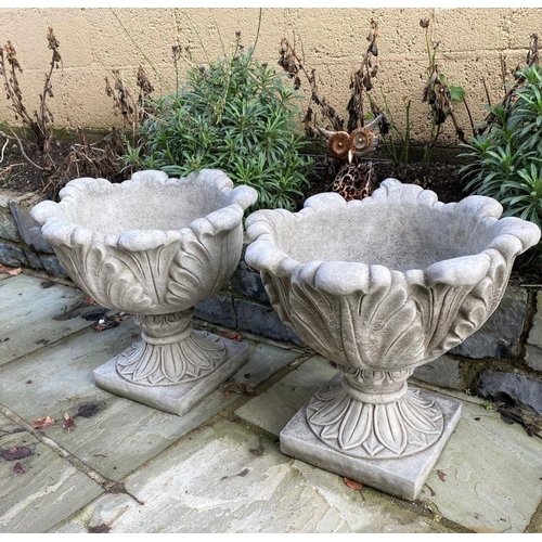 6 - A PAIR OF STONE GARDEN URNS, with turned lip above leaf design to body supported by square platform ... 