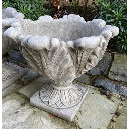 6 - A PAIR OF STONE GARDEN URNS, with turned lip above leaf design to body supported by square platform ... 