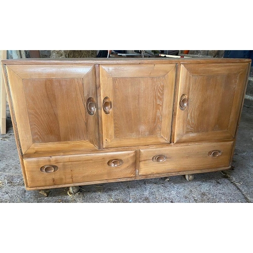 76 - AN ELM WOOD ERCOL THREE DOOR SIDEBOARD, with rectangular top above three doors opening to shelved in... 