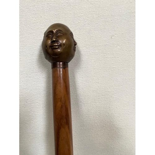 228 - AN UNUSUAL WALKING CANE/STICK; with four face design to the handle, tapered end. 92cm tall.