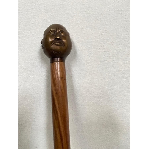 228 - AN UNUSUAL WALKING CANE/STICK; with four face design to the handle, tapered end. 92cm tall.