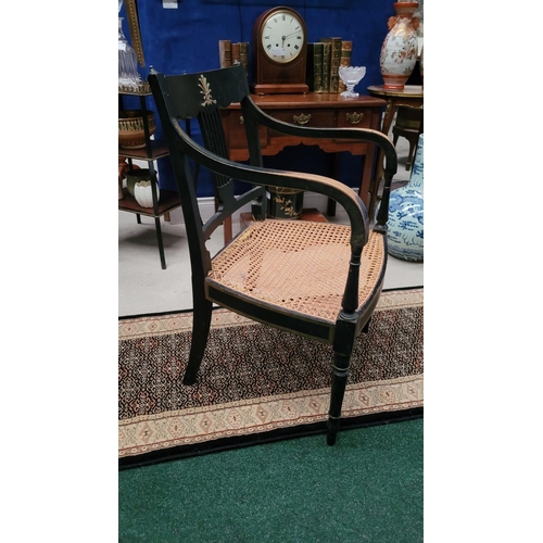 74 - A REGENCY EBONISED CANE-SEAT ARMCHAIR, with gilt mount detail to the curved crest rail and a lyre st... 