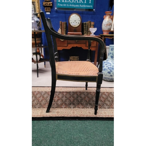 74 - A REGENCY EBONISED CANE-SEAT ARMCHAIR, with gilt mount detail to the curved crest rail and a lyre st... 