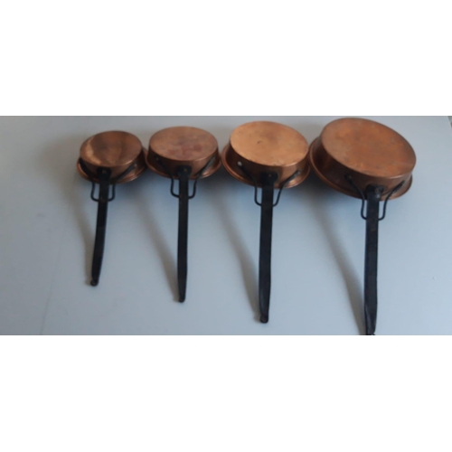 134 - A SET OF FOUR GRADUATED COPPER PANS, with wrought iron handles. Length varies from 50cm to 34cm.