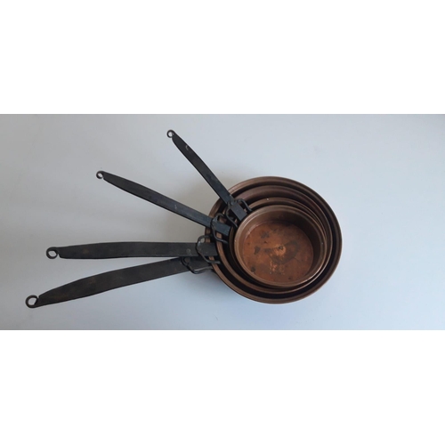 134 - A SET OF FOUR GRADUATED COPPER PANS, with wrought iron handles. Length varies from 50cm to 34cm.