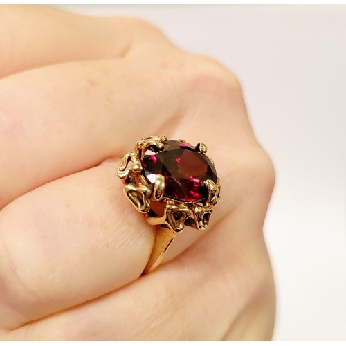 31 - A BEAUTIFUL YELLOW GOLD & GARNET RING, with an open work edge that holds the large oval shaped garne... 