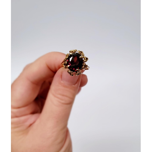31 - A BEAUTIFUL YELLOW GOLD & GARNET RING, with an open work edge that holds the large oval shaped garne... 