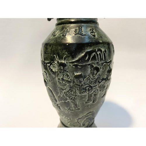 102 - A CHINESE BRONZE URN VASE, with textured fluted design to rim and base, figural design to body in re... 