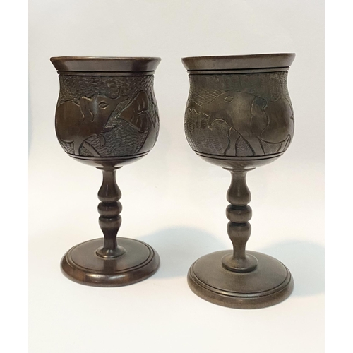 126 - A PAIR OF HARDWOOD CARVED GOBLETS, both with carved scenes to body depicting elephants and with turn... 