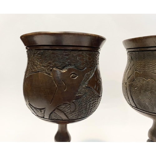 126 - A PAIR OF HARDWOOD CARVED GOBLETS, both with carved scenes to body depicting elephants and with turn... 