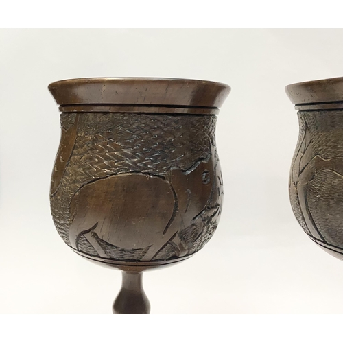 126 - A PAIR OF HARDWOOD CARVED GOBLETS, both with carved scenes to body depicting elephants and with turn... 