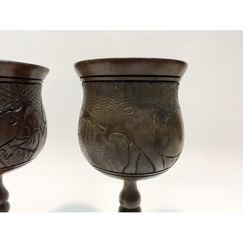 126 - A PAIR OF HARDWOOD CARVED GOBLETS, both with carved scenes to body depicting elephants and with turn... 