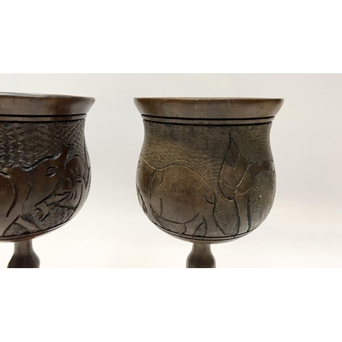 126 - A PAIR OF HARDWOOD CARVED GOBLETS, both with carved scenes to body depicting elephants and with turn... 