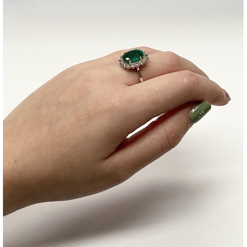 142 - A FANTASTIC 18CT WHITE GOLD EMERALD AND DIAMOND CLUSTER RING, with central vibrant oval cut emerald ... 