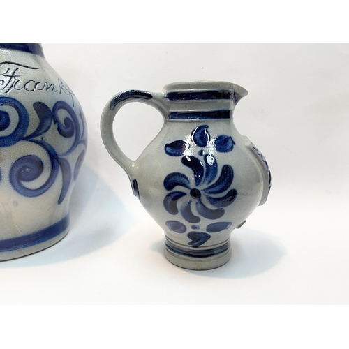 236 - TWO GERMAN SALT GLAZED STONEWARE JUGS, (i) larger pitcher jug with blue painted handle, double band ... 