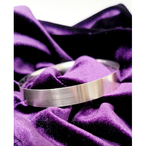 35 - A FINELY CRAFTED COX & POWER STERLING SILVER BANGLE, with brushed finish having a gold coloured stri... 