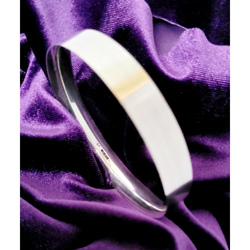 35 - A FINELY CRAFTED COX & POWER STERLING SILVER BANGLE, with brushed finish having a gold coloured stri... 