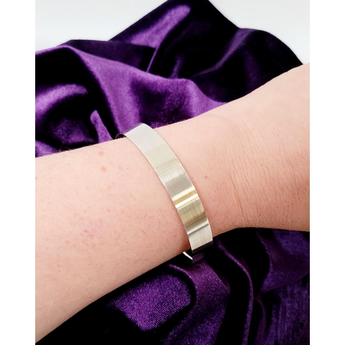 35 - A FINELY CRAFTED COX & POWER STERLING SILVER BANGLE, with brushed finish having a gold coloured stri... 