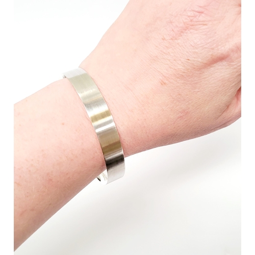 35 - A FINELY CRAFTED COX & POWER STERLING SILVER BANGLE, with brushed finish having a gold coloured stri... 