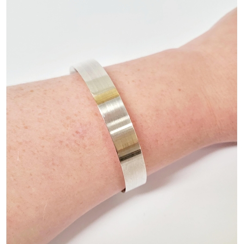 35 - A FINELY CRAFTED COX & POWER STERLING SILVER BANGLE, with brushed finish having a gold coloured stri... 