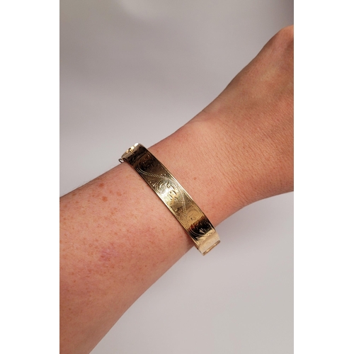 95 - A BEAUTIFUL BRIGHT-CUT DECORATED 9CT YELLOW GOLD BANGLE, the curved bangle is decorated with scrolli... 