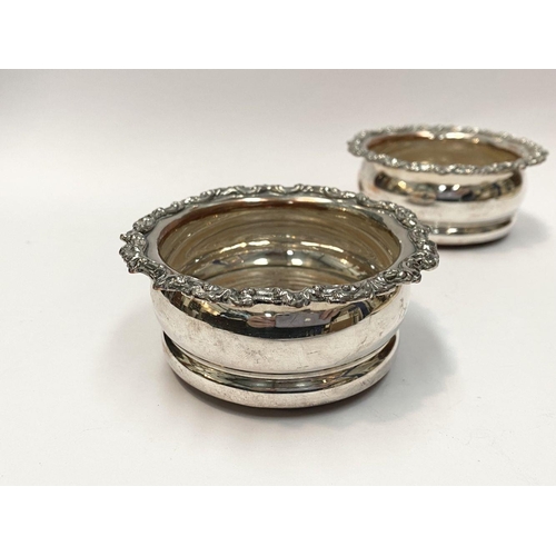 101 - A PAIR OF SMALL VINTAGE SILVER PLATED WINE COASTERS, with decorative floral scrolling borders, hardw... 