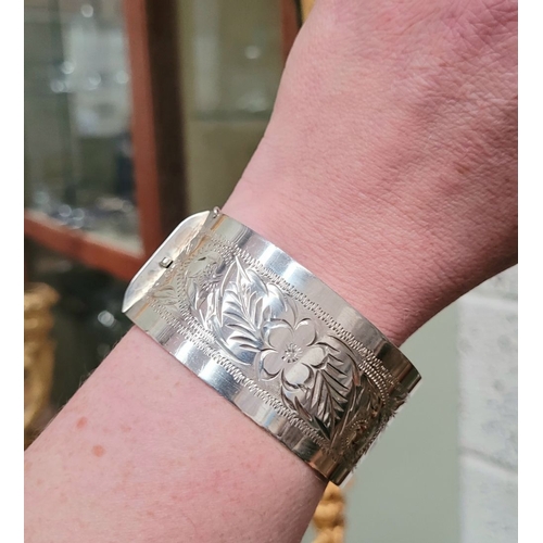 143 - A VERY GOOD QUALITY IRISH SILVER BANGLE, decorated with floral engraved design to one side of exteri... 