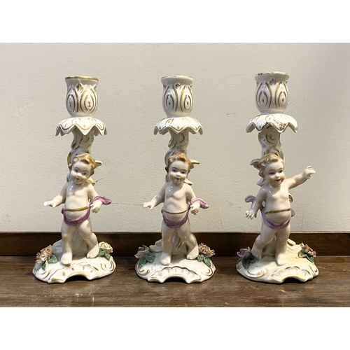 78 - THREE EARLY 20TH CENTURY GERMAN PORCELAIN CHERUB CANDLESTICKS, marked to base with blue mark featuri... 