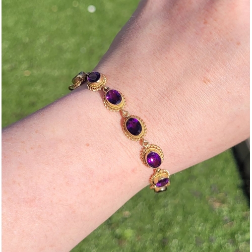 6 - A BEAUTIFUL 9CT YELLOW GOLD AMETHYST BRACELET, 11 oval shaped amethyst stones are set in gold frames... 