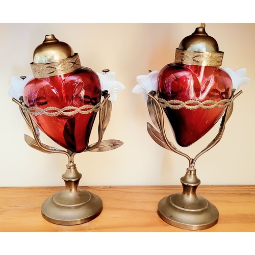 126 - AN UNUSUALLY PAIR OF SACRED HEART VOTIVE LAMPS, each with a cranberry red glass heart that rests wit... 