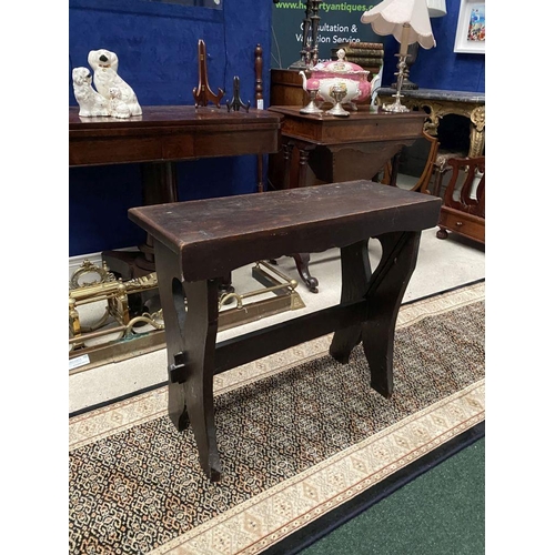 181 - A DARK STAINED HARDWOOD STOOL/BENCH, with shaped supports joined by a cross stretcher. The supports ... 