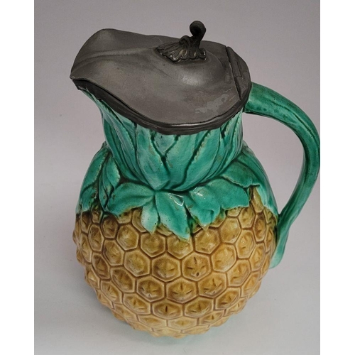 34 - TWO ANTIQUE PEWTER TOPPED JUGS: (i) A lovely antique Majolica style glazed pineapple jug with a hing... 