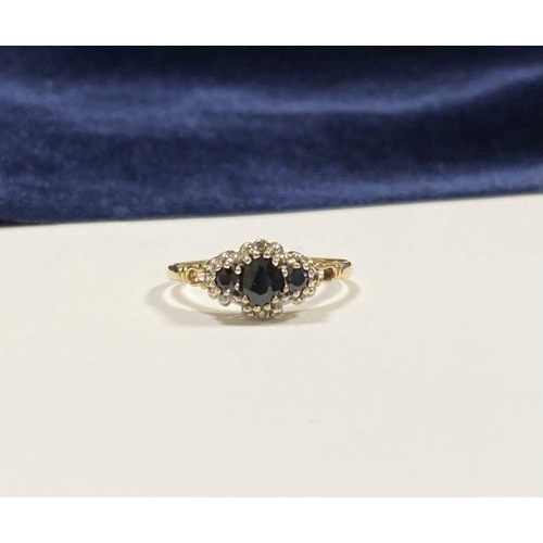 98 - AN ORNATE 9CT GOLD SAPPHIRE AND DIAMOND THREE STONE CLUSTER RING, with central oval cut sapphire fla... 