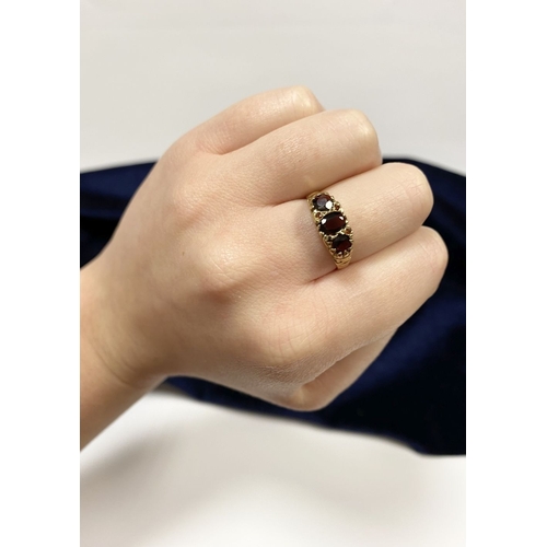 140 - A BEAUTIFUL 9CT YELLOW GOLD THREE STONE GARNET RING, with central oval gut garnet flanked by two rou... 