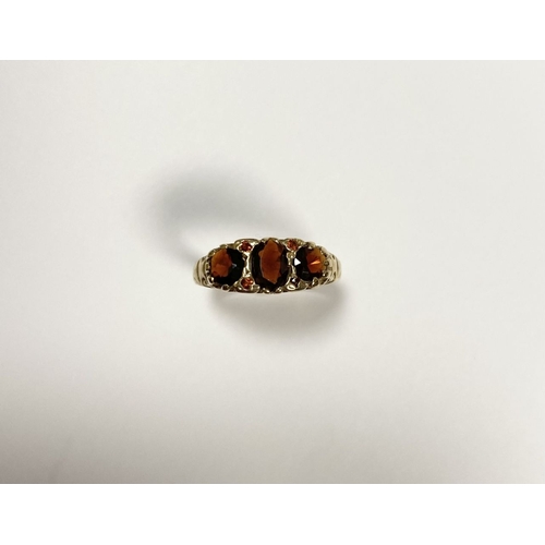 140 - A BEAUTIFUL 9CT YELLOW GOLD THREE STONE GARNET RING, with central oval gut garnet flanked by two rou... 