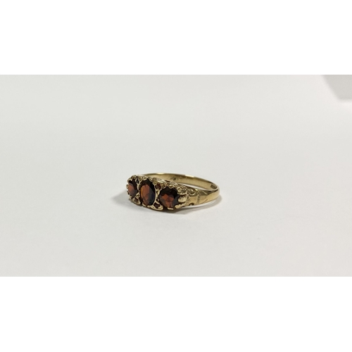 140 - A BEAUTIFUL 9CT YELLOW GOLD THREE STONE GARNET RING, with central oval gut garnet flanked by two rou... 