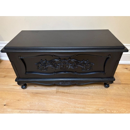 296 - A BLACK PAINTED CARVED CHEST, with moulded border to top, the front with carved foliate design in sh... 