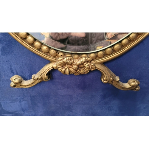 306 - A GILT FRAMED WALL MIRROR, with bevelled glass in an oval shape held within the frame, the frame wit... 