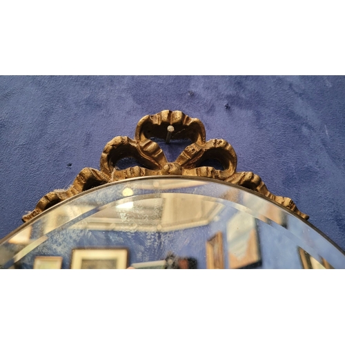 306 - A GILT FRAMED WALL MIRROR, with bevelled glass in an oval shape held within the frame, the frame wit... 