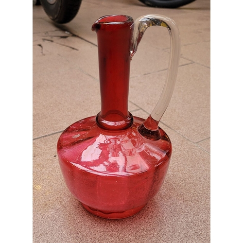 192 - A VERY GOOD ANTIQUE CRANBERRY GLASS DECANTER JUG, with clear glass curved handle, in very good/excel... 