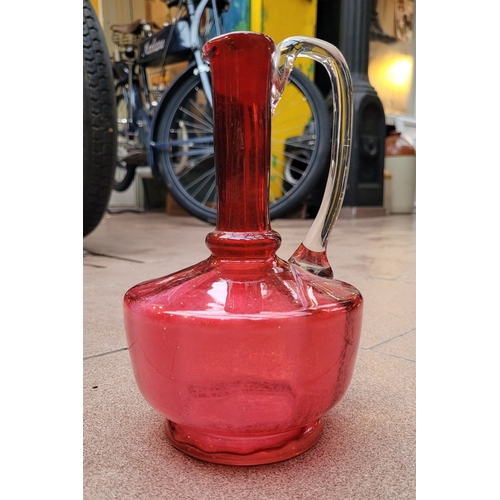 192 - A VERY GOOD ANTIQUE CRANBERRY GLASS DECANTER JUG, with clear glass curved handle, in very good/excel... 