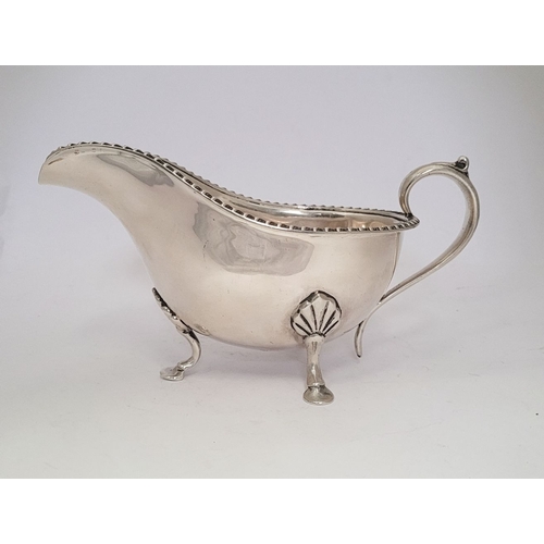 9 - AN IRISH CORK SILVER SAUCE BOAT, with gadrooned edge, a scroll shaped handle resting on a tripod leg... 