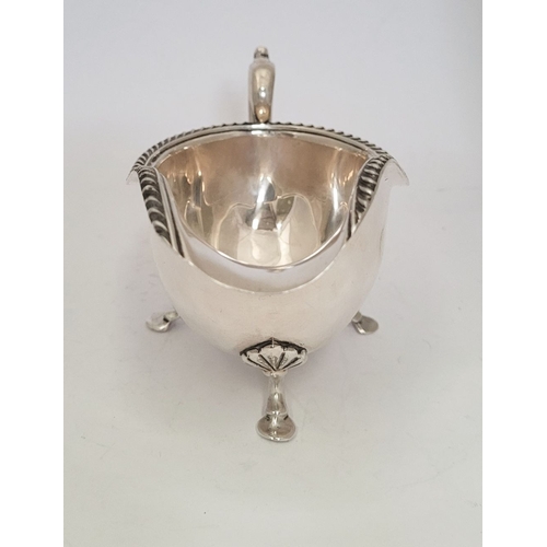 9 - AN IRISH CORK SILVER SAUCE BOAT, with gadrooned edge, a scroll shaped handle resting on a tripod leg... 