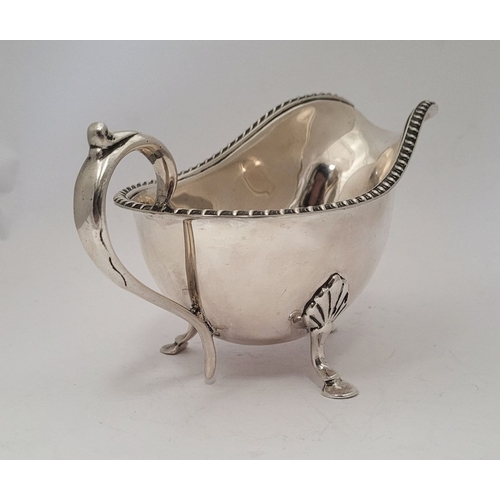 9 - AN IRISH CORK SILVER SAUCE BOAT, with gadrooned edge, a scroll shaped handle resting on a tripod leg... 