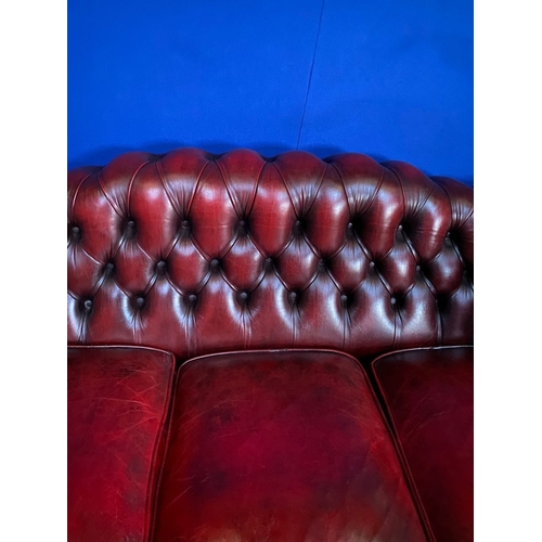 117 - AN EXCELLENT OXBLOOD LEATHER THREE-SEATER CHESTERFIELD COUCH, with arched back and scroll armrests, ... 