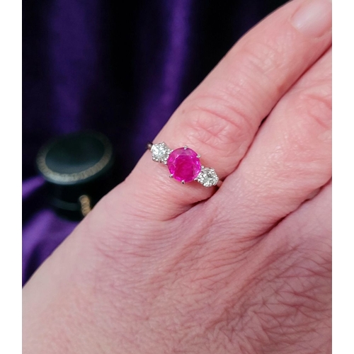 86 - A LOVELY THREE STONE DIAMOND & RUBY RING, with a central bright pink Burma ruby round cut stone, fla... 